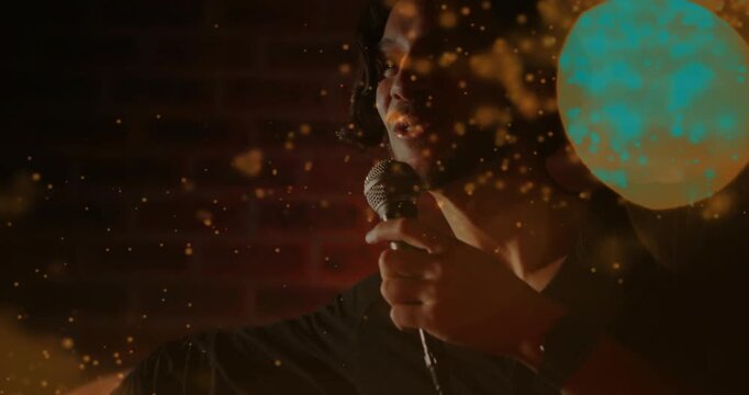 Male singer lifting mic and singing, emoting on music stage, gold particles drifting across face