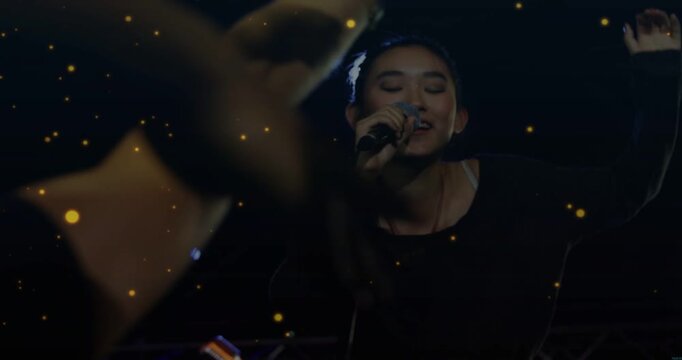 Singer responding to fans reaching, leaning forward, singing into mic on music stage, gold flecks