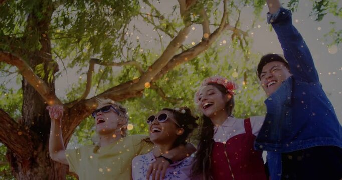 Vertical video: 4 friends linking arms under tree, confetti rising causing arm raises for business