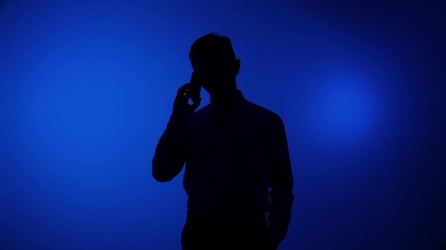 Man silhouette talking on smartphone, communicating and connecting anonymously on a dark blue background, representing concepts of shadow, mystery, and digital interaction