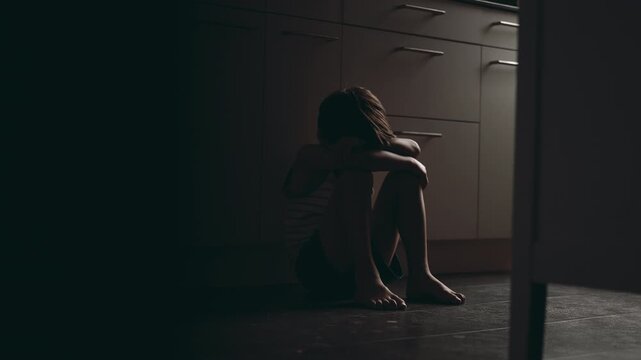 Young boy sitting on kitchen floor hugging knees and burying face in arms showing childhood depression loneliness emotional withdrawal and inner mental health struggle