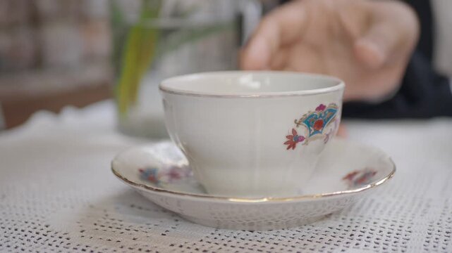Close up footage of antique teacup and saucer being lifted by hand.
