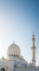 Obraz premium A grand white mosque with multiple domes and a tall minaret under a clear blue sky, showcasing intricate Islamic architecture.