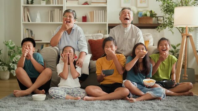Happy Asian multigenerational family watching TV together at home, grandparents and kids laughing, cheering and reacting to game show, joyful bonding, entertainment, fun lifestyle and warm family conn