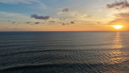 Fototapeta premium Stunning Golden Sunset Over Ocean Horizon with Surfers in the Water at Batu Bolong Beach Bali