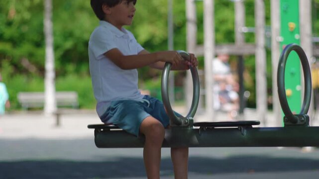 Young boy riding playground bouncing structure while holding metal handles and moving up and down, energetic childhood moment expressing balance coordination and outdoor play