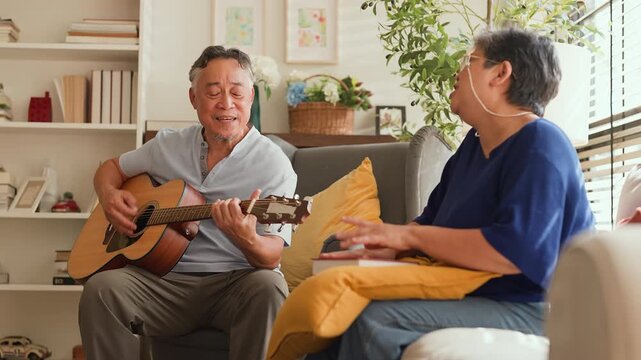 Elderly Asian couple playing guitar and singing together at home, joyful reunion reliving old memories and first date moments, happy retirement lifestyle, love, bonding, music and family connection.