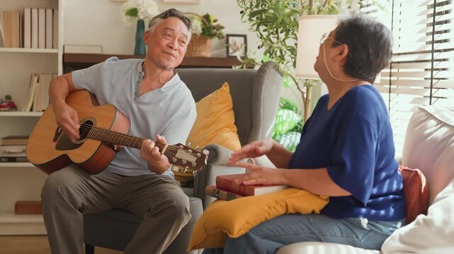 Elderly Asian couple playing guitar and singing together at home, joyful reunion reliving old memories and first date moments, happy retirement lifestyle, love, bonding, music and family connection.