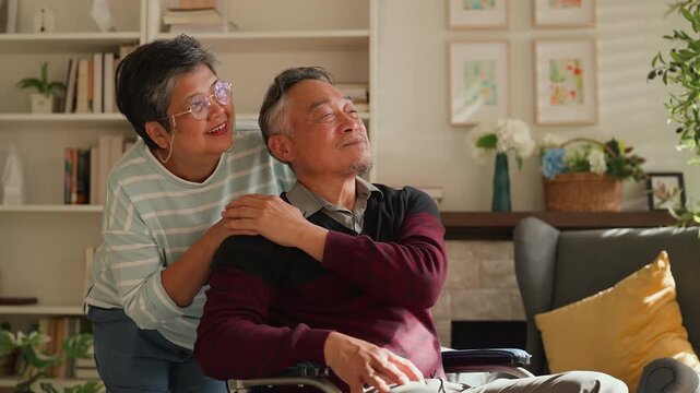 Asian senior couple at home, retired man in wheelchair embraced by loving woman, caregiving support, bonding and true love, warm living room lifestyle, family connection, compassion and lifelong partn