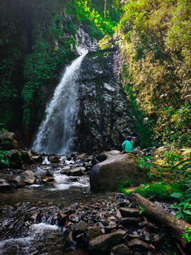 Person Sitting on Rock Watching Tropical Waterfall in Lush Jungle &ndash; Nature Adventure and Mindfulness Concept