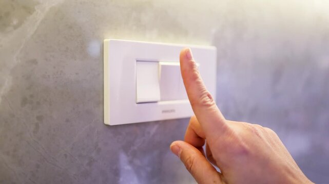 Close Up of Finger Pressing White Light Switch on Marble Wall