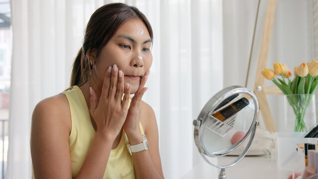 Young adult woman gen z black asia people relax get ready prepare clean makeup apply cream skin care make up getting dressed at home. Look at mirror camera self love anti aging health happy vanity.