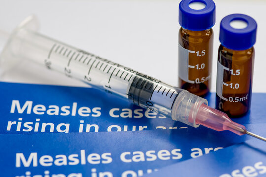 A measles outbreak and vaccination concept with a macro closeup of information leaflets, a syringe needle and medical liquid containers