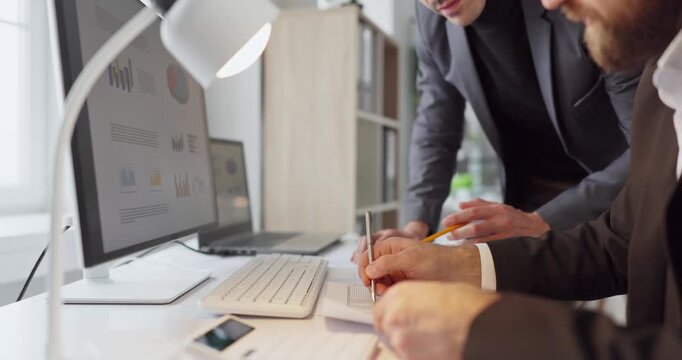 Men coworkers in office conduct finance analysis. They study charts on a computer and refine strategy while preparing a meeting report with figures. Concept teamwork in financial analysis.