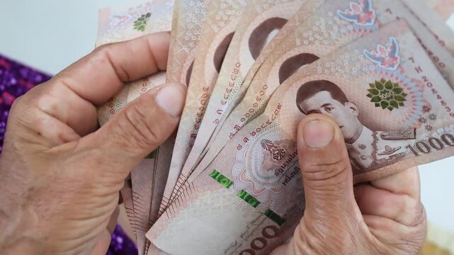 Elderly hands counting Thai banknotes Baht, Money close-up. Concept of retirement savings, pension income, financial security, budgeting, and senior financial planning