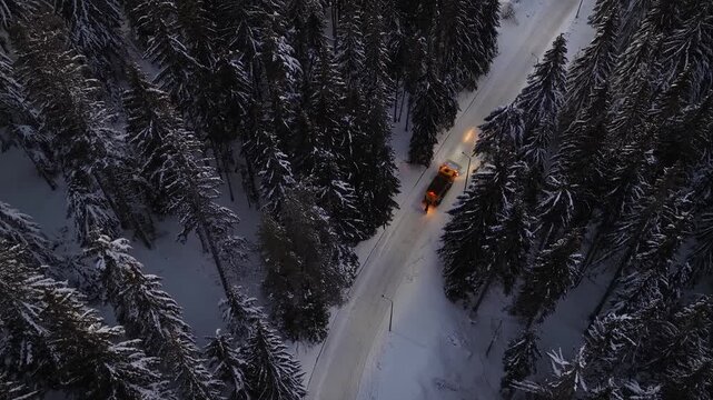 Professional Services snow plow truck maintaining safe road conditions under streetlights during nighttime and clear mountain ski resort snow covered roads after heavy winter storm snowfall