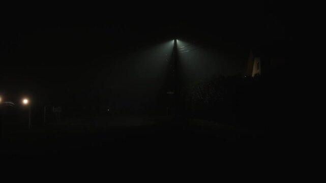 Quiet foggy residential street at night with street lamp creating dark cinematic atmosphere of empty neighborhood with diffused fog light and sense of isolation