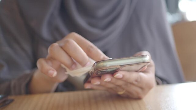 Close up of woman cleaning smartphone with wet wipe for hygiene.
