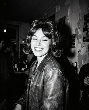 Joyful Woman in Leather Jacket Laughs with Eyes Closed at Bar or Party