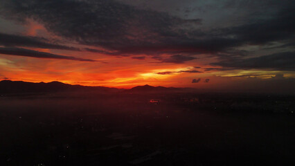 Obraz premium Breathtaking Sunset Over Mountain Range with Fiery Sky and Hazy Valley Landscape