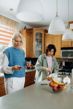 In a warm, inviting kitchen filled with wooden cabinets, two friends share a joyful moment.