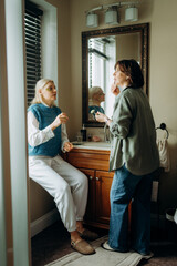 Fototapeta premium Two women share a joyful moment in a warm bathroom. One applies makeup while the other sits calmly. Soft morning light fills the space, creating a friendly and intimate atmosphere.