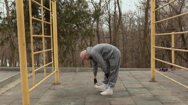 Full body shot of sportsman in grey tracksuit performing toe touch stretching on sports ground. Athlete warming up his back and hamstrings before training outdoors