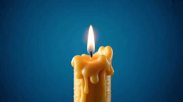 Single yellow candle with bright flame and dripping wax on blue background