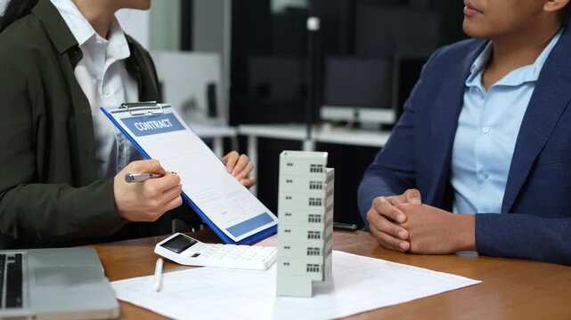 Real estate broker agent presenting and consult to customer to decision making sign insurance form agreement, home model, concerning mortgage loan offer in office.