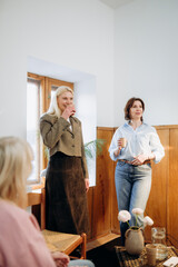 Obraz premium A cozy gathering unfolds in a bright room as two women chat joyfully while sipping warm drinks. The atmosphere is friendly, filled with laughter and genuine connections among friends.