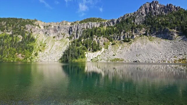 Footage of the stunning landscape along the Tolmie Peak Trail in Mount Rainier National Park, Washington. The view captures the clear, emerald waters of Eunice Lake reflecting the rugged cliffs and lu