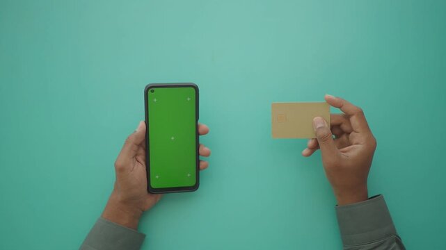 Person holding smartphone with green screen next to credit card for payment.