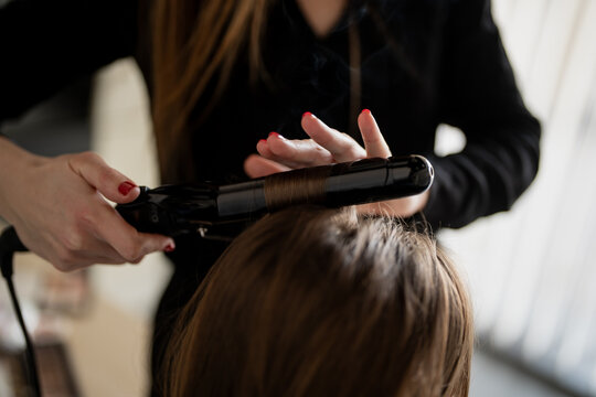 Hair stylist using flat iron on client hair in salon, showing professional beauty service, personal care routine, and modern grooming business