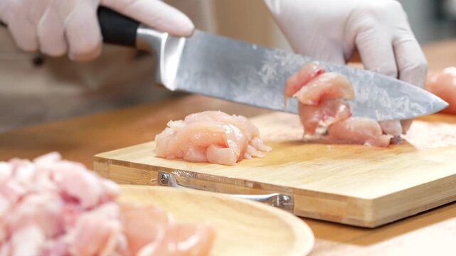 hands slicing raw pork on a wooden board in the kitchen, preparing to cook.
