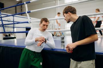 Fototapeta premium Boxers discuss training techniques and strategies while checking the time during a busy practice session. The mood is friendly yet competitive, showcasing dedication to the sport.