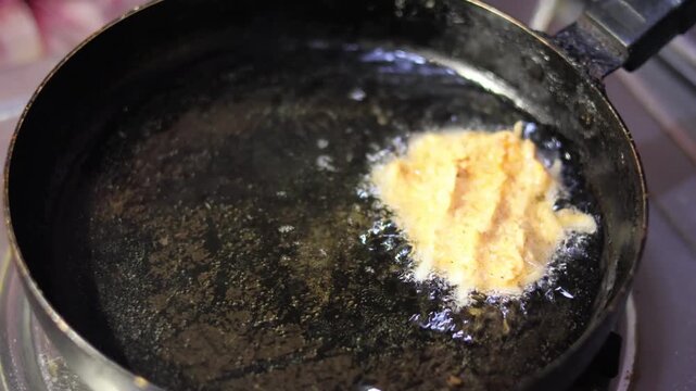 Traditional Indian potato bondas deep frying in hot golden oil inside a metal pan.