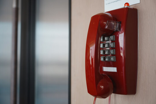 Red vintage wall-mounted telephone with numeric keypad and handset in indoor setting