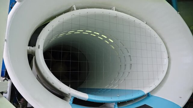 Interior view of an aerodynamic wind tunnel test section featuring an elliptical duct with grid screening, flow-conditioning panels, and an axial fan in an engineering facility