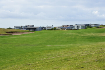 Naklejka premium South Africa,Golf Resort,A wide green golf course with modern buildings in the background under a cloudy sky