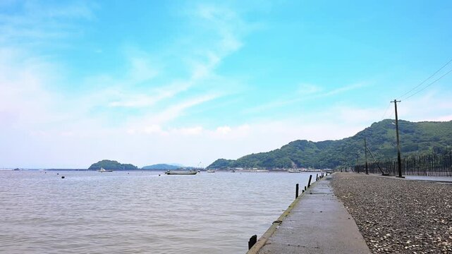 海へ消える道：干潮時にのみ現れる幻想的な風景
「熊本県宇土市に位置する『長部田海床路』。潮の満ち引きによって海の中から現れるこの道は、海苔養殖などの漁業のために作られました。広大な有明海と青い空、そして海へと続く電柱が織りなすノスタルジックな日本の絶景を捉えた映像素材です。」
宇土市住吉(長部田海床路)
A Road That Disappears into the Sea