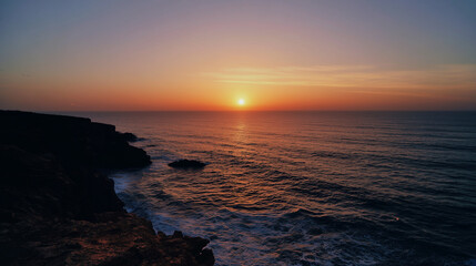 Obraz premium The edge of a cliff at sunset with the sun dipping below the horizon of the sea