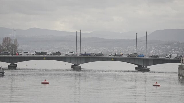 Zurich, Switzerland March 28, 2026: Red kayak paddling on lake zurich with city traffic on quaibrucke bridge on a cloudy day
