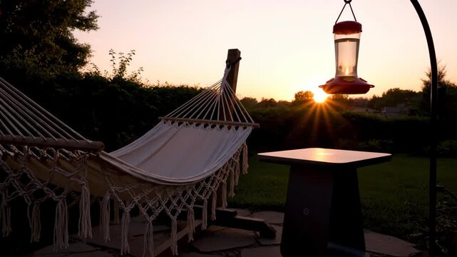 Peaceful sunset with hammock and hummingbird feeder in backyard garden. Relaxation, nature, and summer lifestyle concept.
