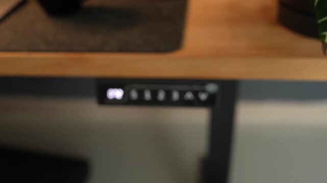 Close up of hand pressing buttons on adjustable standing desk controal panel to change height