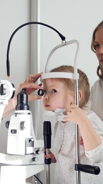 Child's ophthalmologist checks little girl's eyesight - mother and daughter in ophthalmology clinic