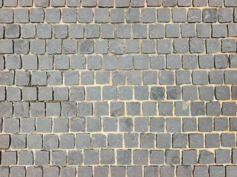 Top down view of a dark grey cobblestone pavement pattern with square stones and light mortar