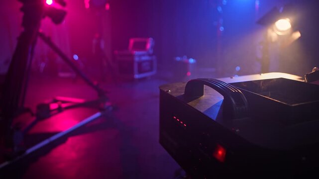 Close view of a stage fog machine with smoke on a dim backstage set with colorful lights and camera equipment. Concept of concert production, theater effect, filming, entertainment, event technology.