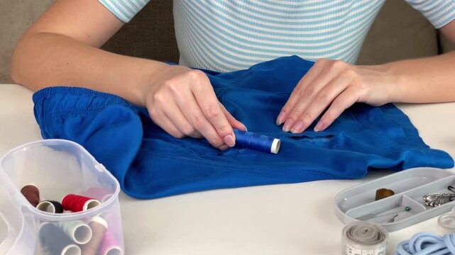 A girl picks up a spool of thread to repair a pair of torn shorts. Concepts of sewing, home repair, handicrafts, and home care.