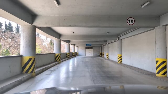 Driving pov inside a multi story parking garage concrete ramp with yellow and black striped columns, entering a modern empty building car park for safe vehicle storage