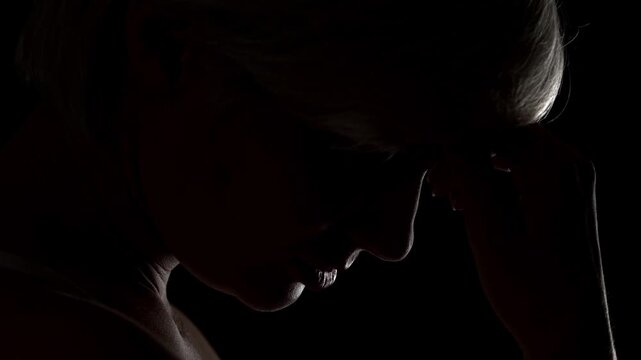 Close up cinematic profile of a young blonde woman slowly raising her head from a sad or contemplative pose with dramatic lighting
